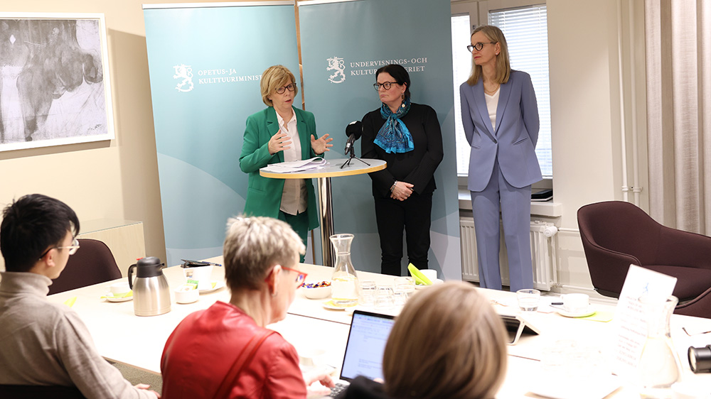 Ministeri Henriksson sekä selvitystyön laatineet dosentti Taina Juurakko-Paavola ja opetusneuvos, FT Yvonne Nummela seisovat median edessä luovutuksen jälkeen.
