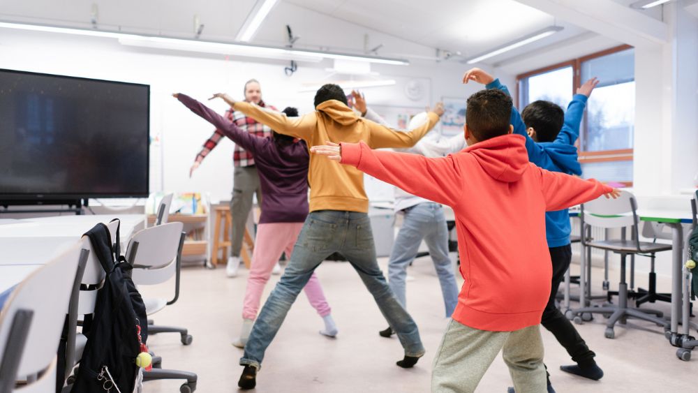 Oppilaat tekevät haarahyppyjä luokkahuoneessa opettajan johdolla.