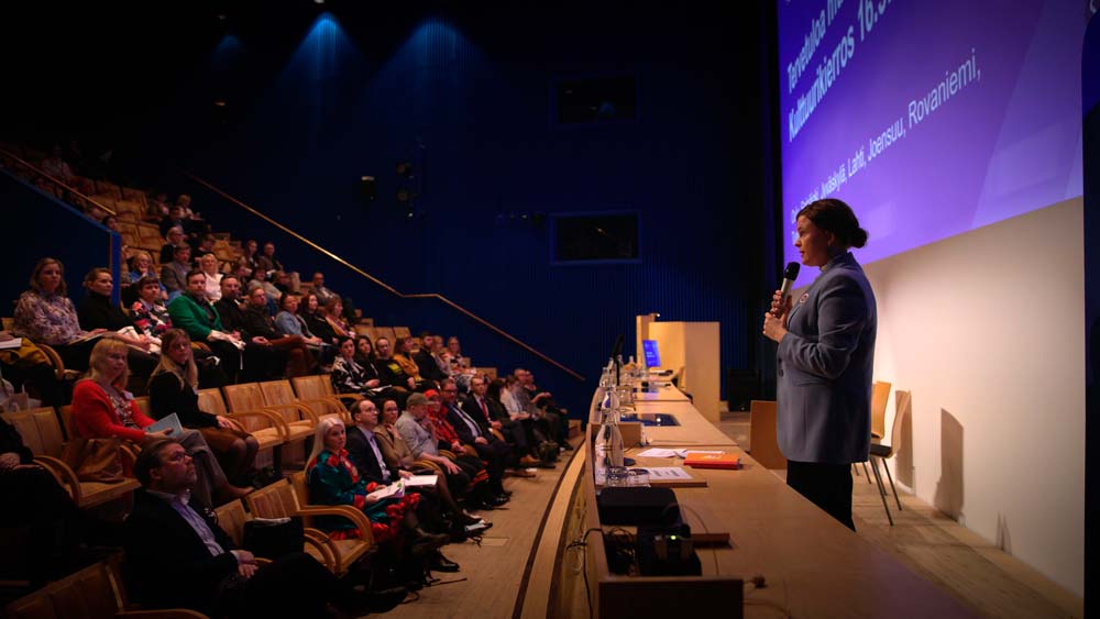Ministeri Talvitie puhuu yleisön edessä auditoriossa.
