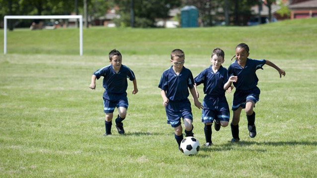 Pojat pelaavat jalkapallo kentällä.