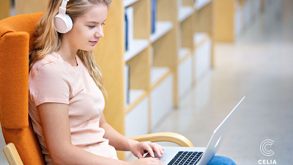 Tyttö istuu kirjastossa kannettava tietokone sylissään ja kuulokkeet korvillaan. Alakulmassa Celian logo.